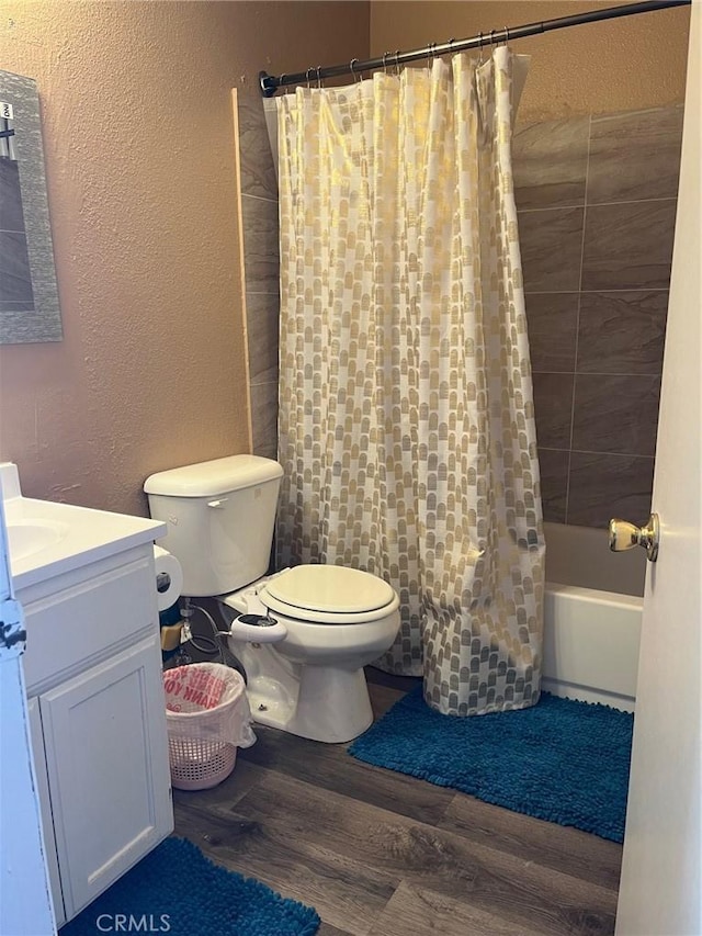 full bath featuring shower / bath combo, wood finished floors, vanity, toilet, and a textured wall