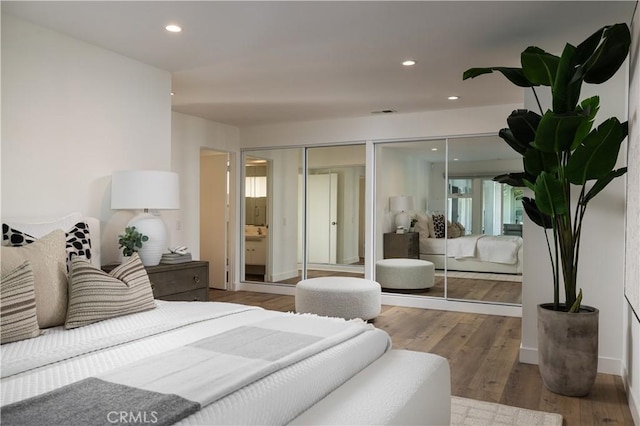 bedroom featuring visible vents, wood finished floors, two closets, baseboards, and recessed lighting