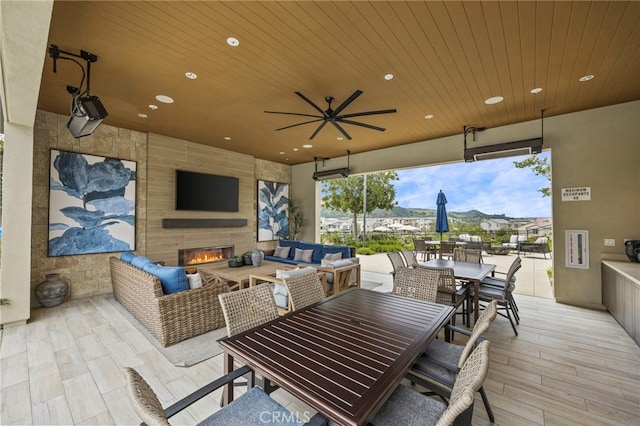 view of patio with outdoor dining area, ceiling fan, and an outdoor living space with a fireplace