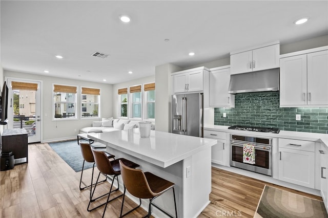 kitchen featuring visible vents, open floor plan, white cabinetry, under cabinet range hood, and appliances with stainless steel finishes