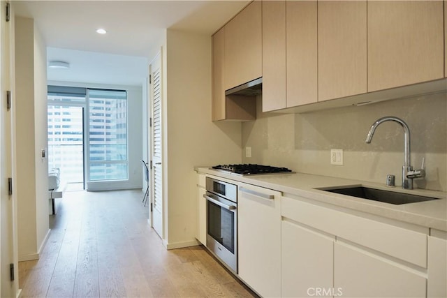 kitchen with oven, light wood-style floors, light countertops, gas stovetop, and a sink