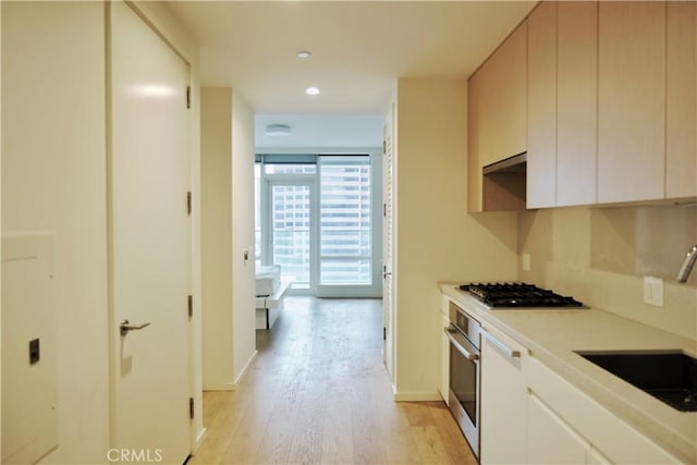 kitchen featuring a sink, baseboards, light wood-style flooring, and oven