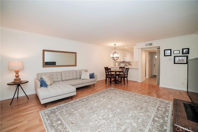 living room featuring an inviting chandelier, ornamental molding, light wood finished floors, and visible vents