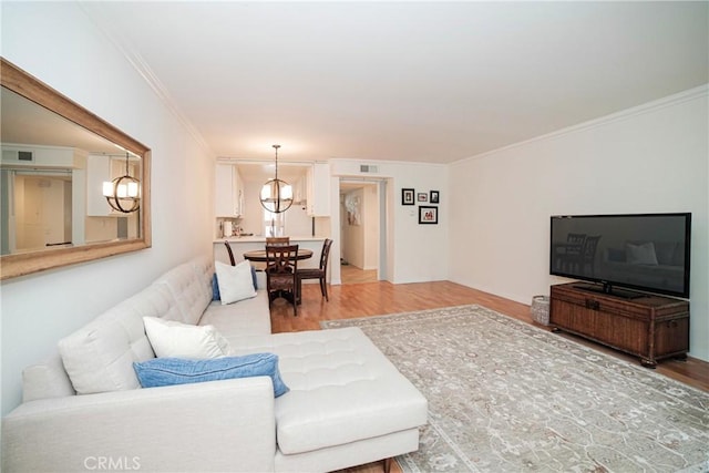 living area with visible vents, ornamental molding, and light wood-style flooring