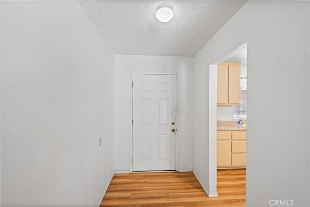 doorway to outside featuring light wood-style floors, a textured ceiling, and baseboards