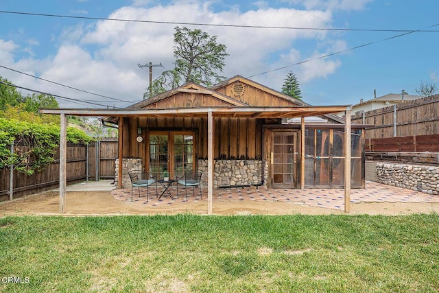 rear view of property with stone siding, a patio, a fenced backyard, board and batten siding, and a lawn