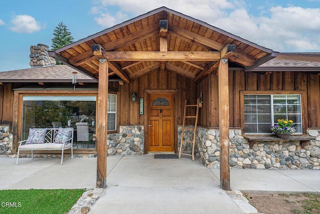 view of exterior entry with a shingled roof, board and batten siding, and stone siding