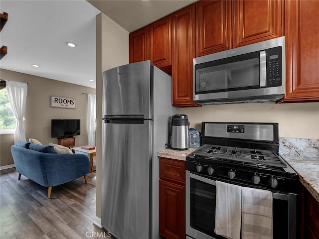 kitchen with wood finished floors, open floor plan, recessed lighting, light stone counters, and appliances with stainless steel finishes