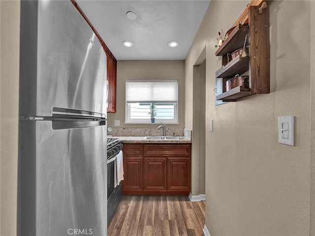 kitchen with open shelves, light stone countertops, a sink, light wood-style flooring, and appliances with stainless steel finishes