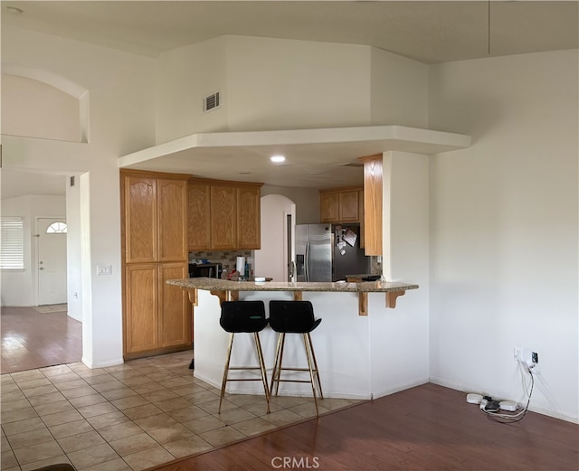 7548 Chase Ave, Hesperia, CA 92345 - kitchen with stainless steel fridge with ice dispenser, a peninsula, a towering ceiling, a kitchen breakfast bar, and stone countertops