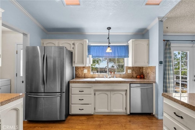 kitchen featuring crown molding, a sink, stainless steel appliances, light wood-type flooring, and backsplash