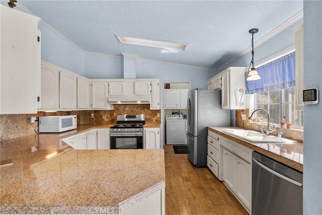 kitchen featuring appliances with stainless steel finishes, a sink, tile countertops, washer / dryer, and under cabinet range hood