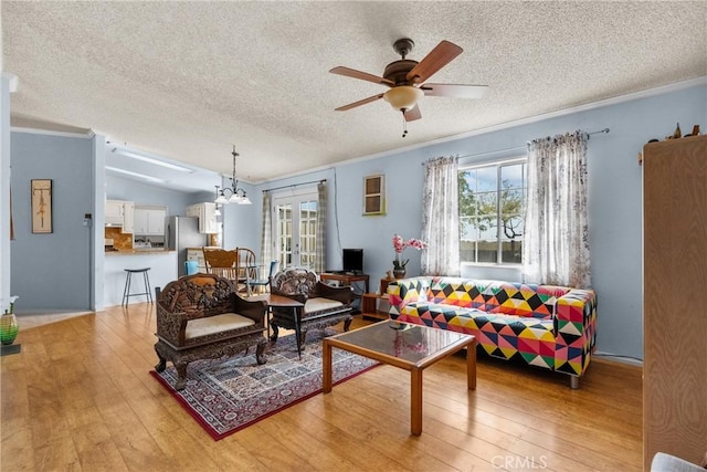 living area featuring ornamental molding, ceiling fan with notable chandelier, light wood finished floors, and a textured ceiling