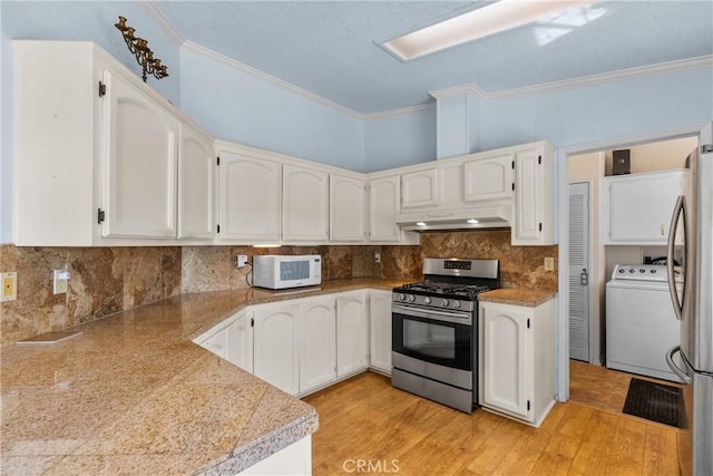 kitchen with appliances with stainless steel finishes, tile countertops, washer / dryer, under cabinet range hood, and ornamental molding