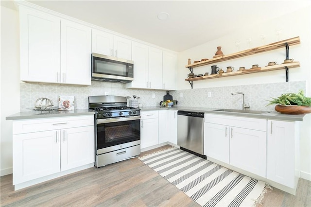 kitchen featuring tasteful backsplash, open shelves, light wood-type flooring, a sink, and stainless steel appliances