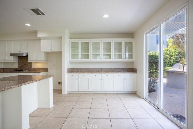 kitchen with visible vents, black stovetop, stone countertops, glass insert cabinets, and white cabinetry