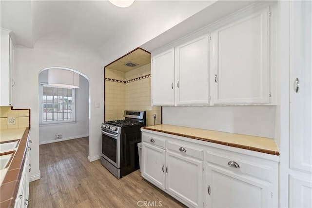 3712 Virginia Rd, Los Angeles, CA 90016 - kitchen with arched walkways, light countertops, white cabinets, light wood finished floors, and stainless steel range with gas cooktop