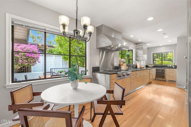 kitchen with stainless steel gas cooktop, dark countertops, beverage cooler, wall chimney exhaust hood, and a chandelier