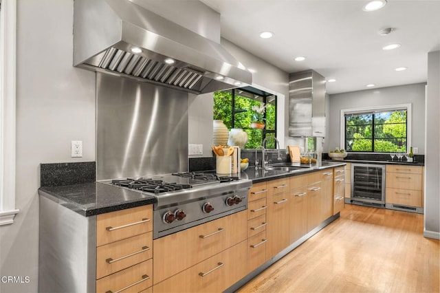 kitchen with wine cooler, stainless steel gas cooktop, light wood-style floors, wall chimney range hood, and a sink