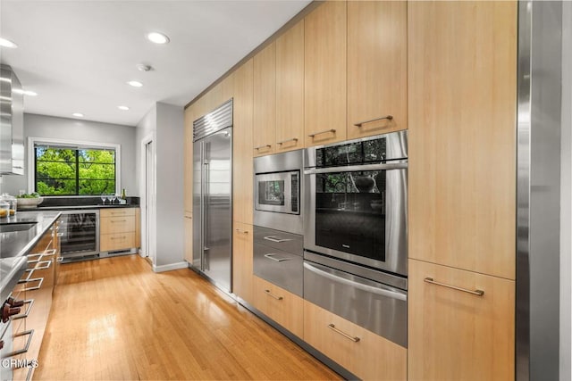 kitchen featuring a warming drawer, light brown cabinetry, light wood-type flooring, wine cooler, and built in appliances