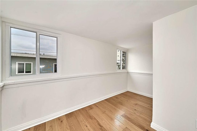 spare room featuring baseboards, wood finished floors, and a healthy amount of sunlight