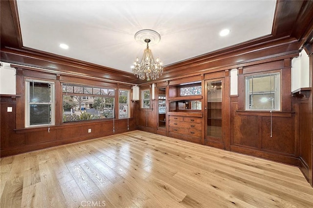 unfurnished dining area with crown molding, an inviting chandelier, wood-type flooring, wood walls, and recessed lighting