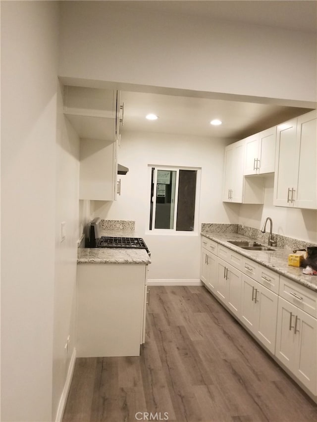 kitchen with wood finished floors, white cabinetry, light stone counters, a sink, and gas stove
