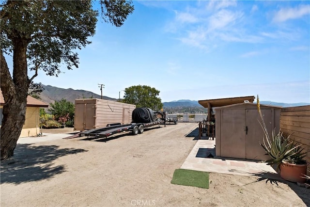 view of yard with an outbuilding, a mountain view, a storage shed, and fence