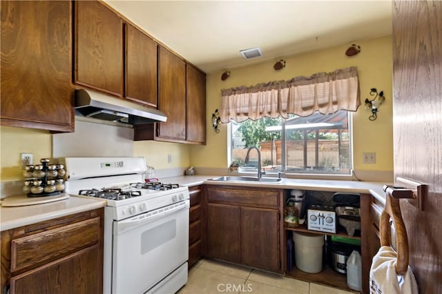kitchen with white gas range, light countertops, under cabinet range hood, a sink, and light tile patterned floors