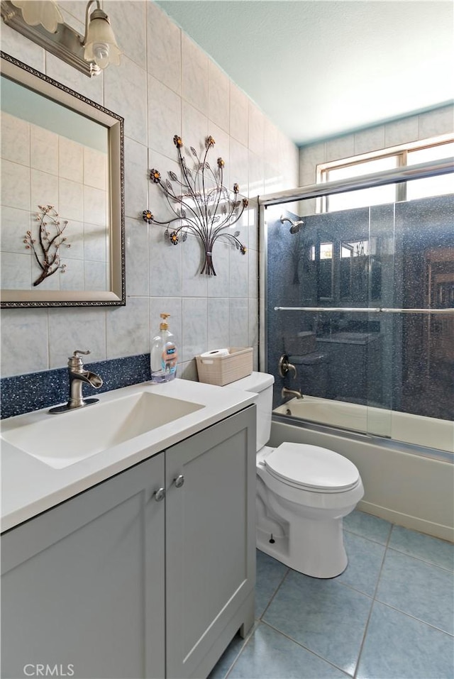 full bath featuring vanity, tile patterned flooring, toilet, tile walls, and bath / shower combo with glass door