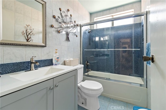bathroom featuring tile patterned flooring, vanity, toilet, tile walls, and bath / shower combo with glass door