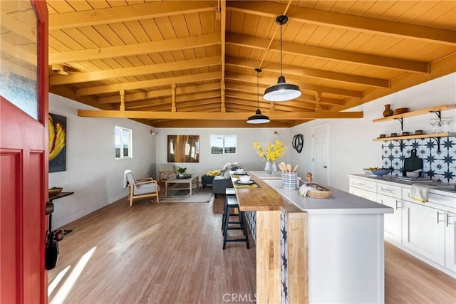 kitchen with light wood-type flooring, lofted ceiling with beams, white cabinets, and a kitchen island