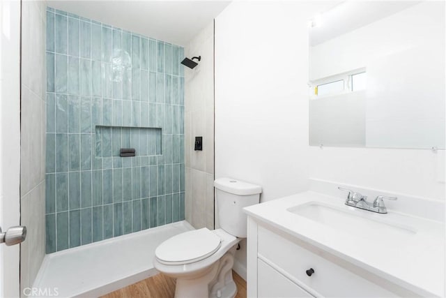 bathroom with vanity, a tile shower, toilet, and wood finished floors