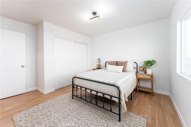 bedroom with a closet, baseboards, multiple windows, and light wood-style floors