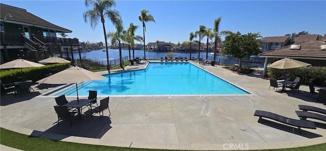 community pool with a water view, a patio area, and fence