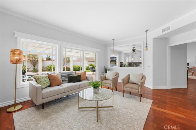 living room featuring crown molding, ceiling fan, baseboards, wood finished floors, and visible vents