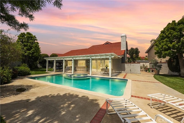 pool at dusk featuring a patio, a pool with connected hot tub, and a pergola