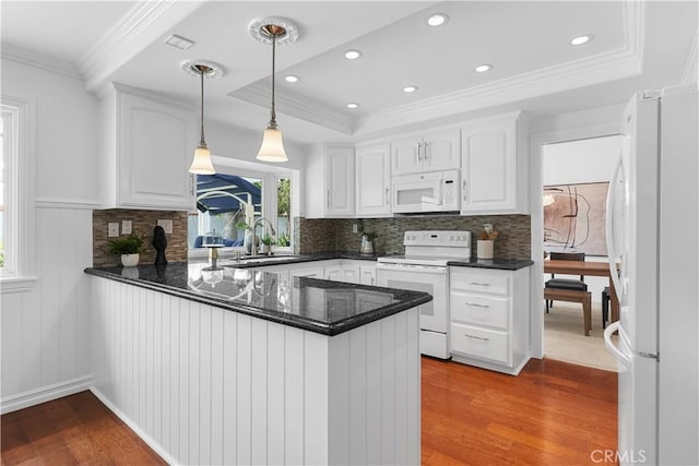 kitchen with wood finished floors, a sink, white cabinets, a peninsula, and white appliances