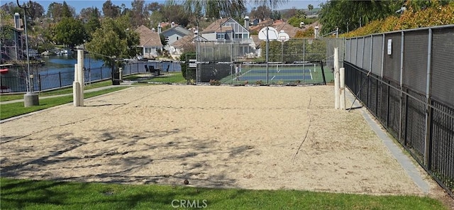 view of community with fence, a tennis court, a water view, and volleyball court