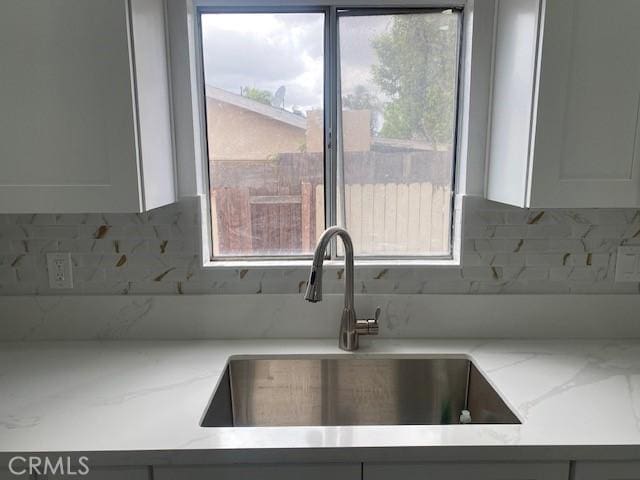 kitchen with a sink, light stone countertops, and backsplash