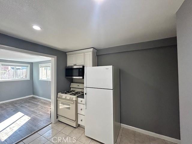 kitchen featuring white appliances, white cabinetry, baseboards, and light tile patterned flooring