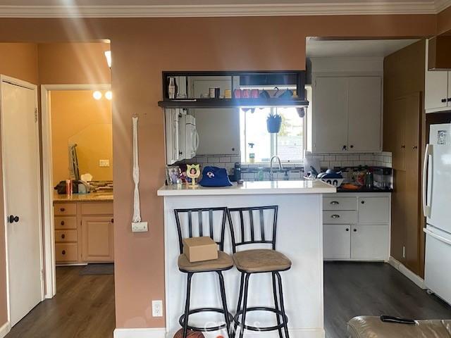 kitchen featuring freestanding refrigerator, backsplash, a breakfast bar, and dark wood-type flooring