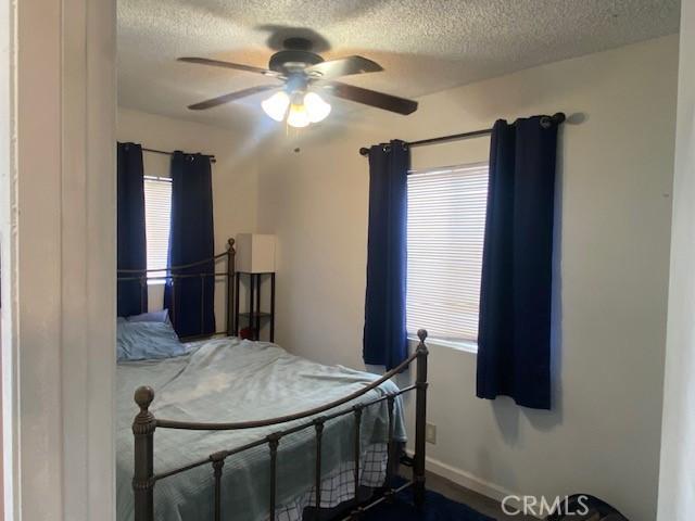bedroom featuring baseboards, a ceiling fan, a textured ceiling, and multiple windows