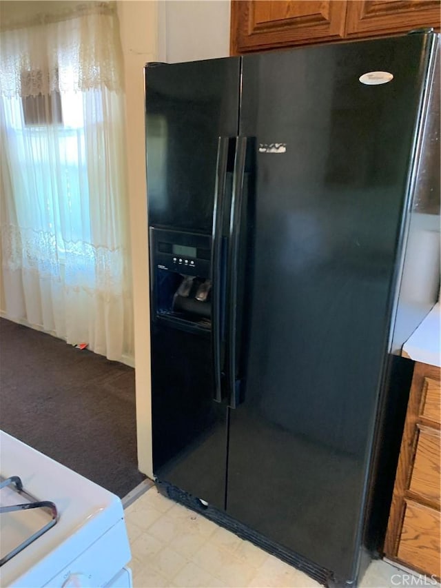 kitchen featuring brown cabinetry, light floors, black refrigerator with ice dispenser, and light colored carpet