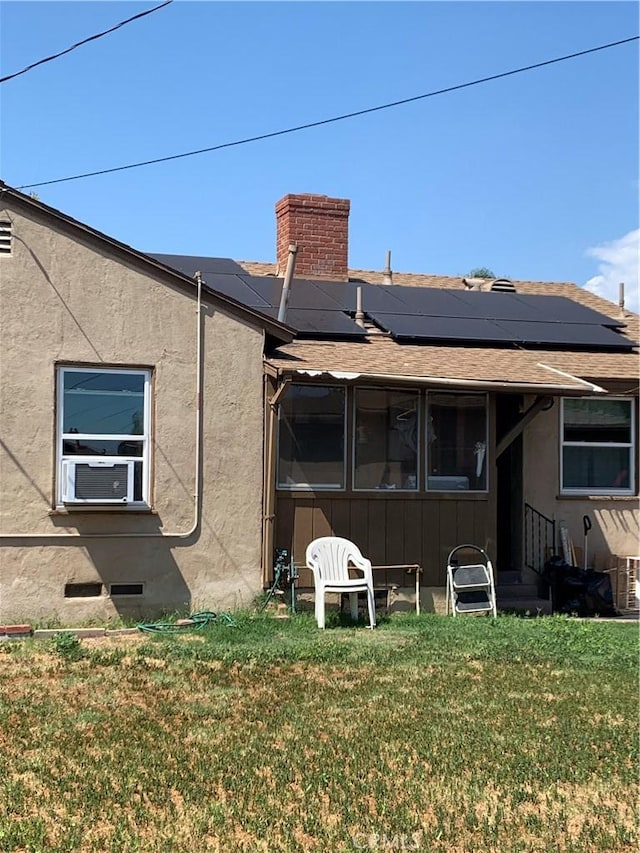 back of house with a chimney, a lawn, cooling unit, roof mounted solar panels, and a shingled roof