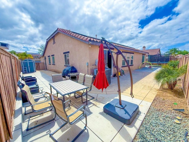 view of patio featuring outdoor dining area, an outdoor structure, a fenced backyard, and a storage unit
