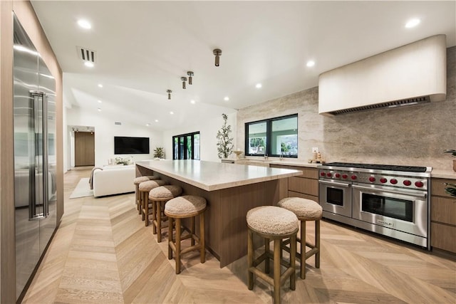 kitchen featuring wall chimney range hood, high quality appliances, light countertops, a kitchen island, and visible vents