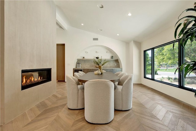 dining area with a glass covered fireplace, recessed lighting, baseboards, lofted ceiling, and visible vents
