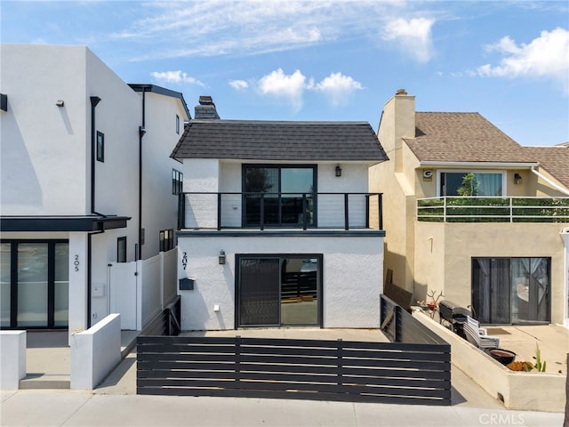 back of property with a chimney, a gate, fence, a balcony, and stucco siding