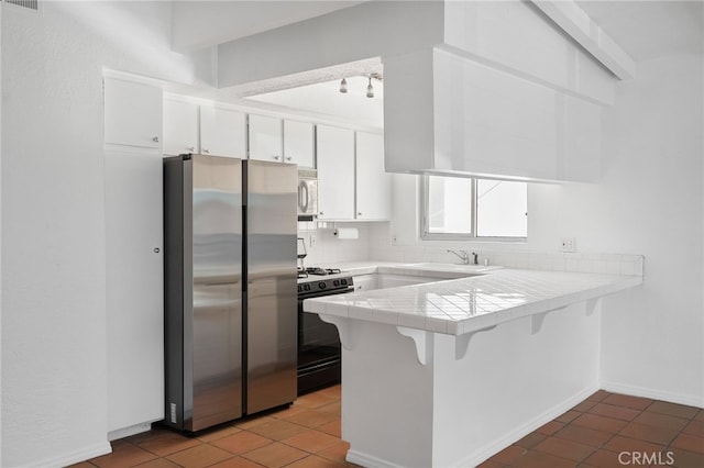 kitchen featuring gas stove, tile counters, freestanding refrigerator, a peninsula, and white microwave